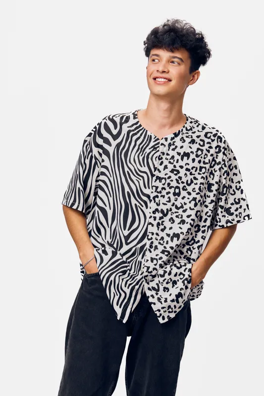 young man smiling wearing animal print t-shirt with zebra and leopard patterns, casual style, black pants, modern fashion, standing on white background