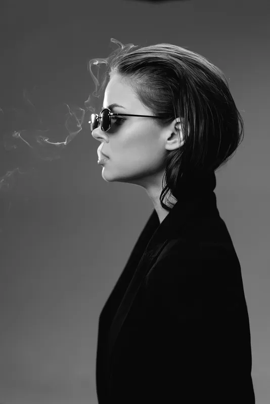 Stylish woman smoking in black and white with sunglasses and short hair, expressing calm confidence with smoke effect