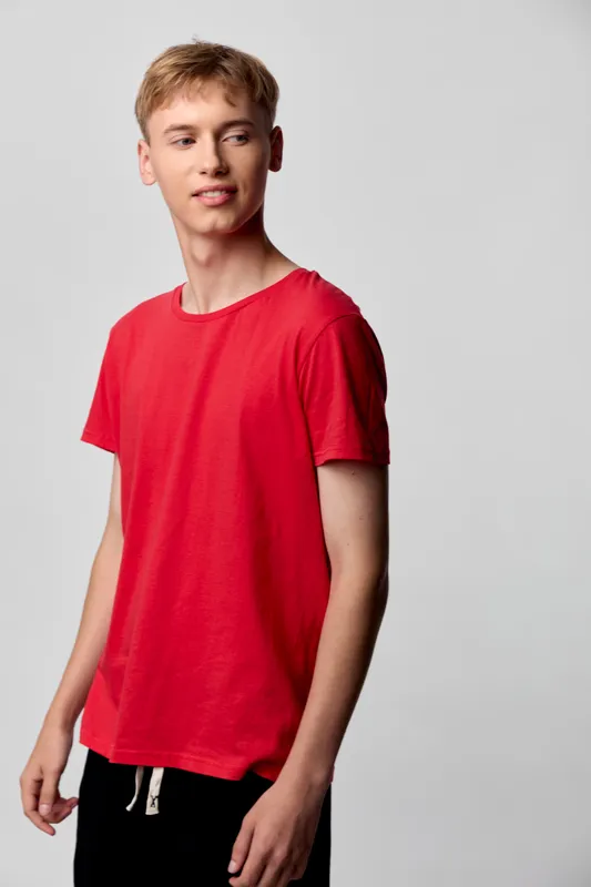 Boy in a red t shirt poses in a studio, casual youth fashion with a relaxed stance, clean background, ideal for modern apparel catalogs and teen wardrobe inspiration
