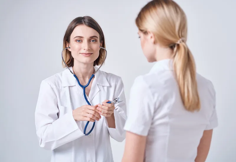Врач в медицинском халате на светлом фоне и пациентка — блондинка