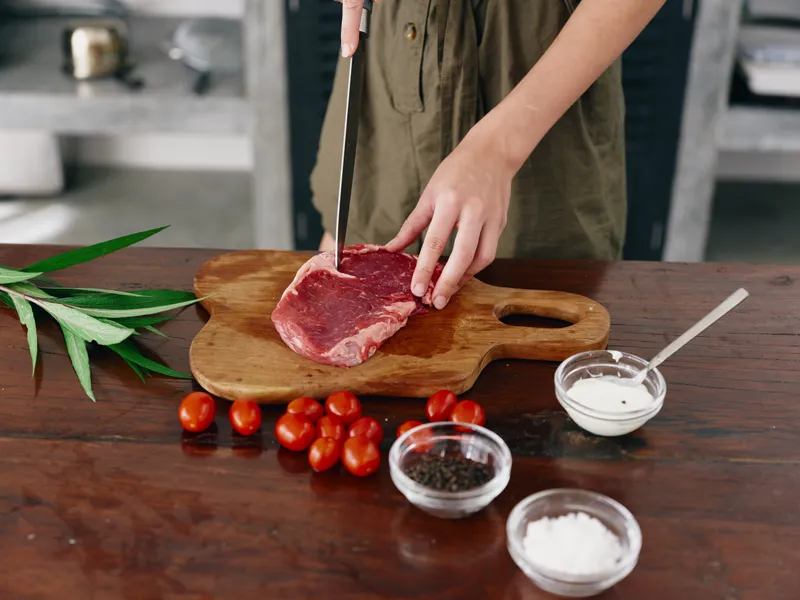 Женщина с ножом в руке нарезает стейк из мяса для жарки на кухне