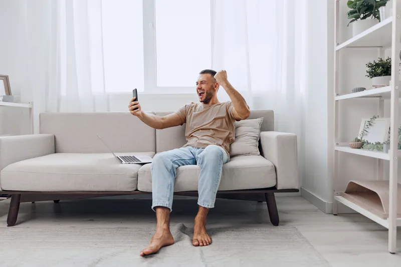 Excited man celebrating success while on a phone call, embracing his emotions and enjoying the moment of connection in a cozy home environment.