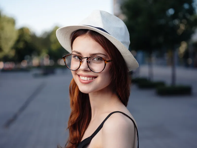 Счастливая женщина в белой шляпе и очках гуляет на природе по улице