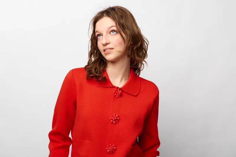 Young woman in red knitted sweater looks up thoughtfully on white background. Casual fashion, portrait, and natural expression concept with soft studio lighting and simple composition.