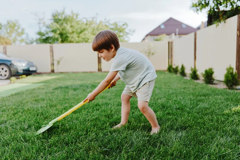 Young boy gardening with a vibrant yellow shovel, enjoying outdoor activity, sunny day, and connecting with nature. Playful and energetic scene in a green lawn.