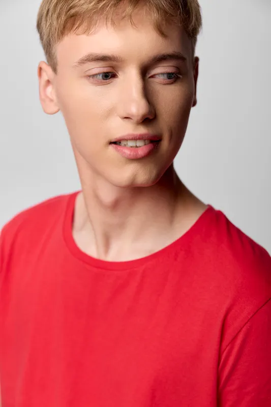 Young man in a red shirt with a sideways gaze in a studio casual setting, a clean headshot conveying modern fashion and confident relaxed vibe