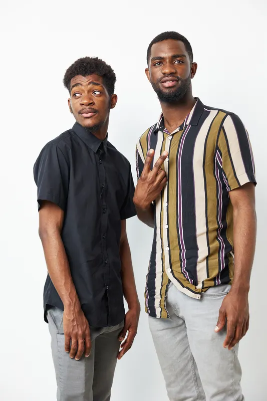 Two young African American men posing playfully together, showcasing their trendy outfits and confident expressions. A stylish photo capturing friendship and style.