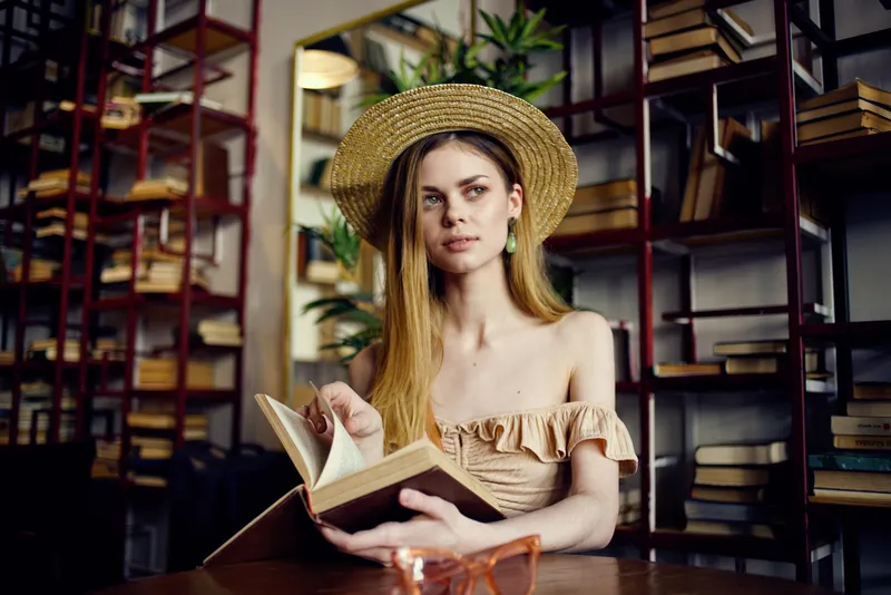 Симпатичная женщина в шляпе с книгой читает во время отдыха в помещении