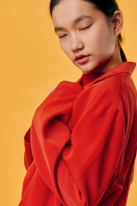 Woman with eyes closed wearing oversized red sweater on orange background for fashion portrait, style and cozy casual clothing. Young female model with relaxed expression and trendy outfit.