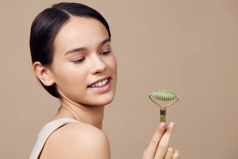 Young woman holding a jade face roller, promoting skincare and self care, showcasing natural beauty and relaxation in a neutral background