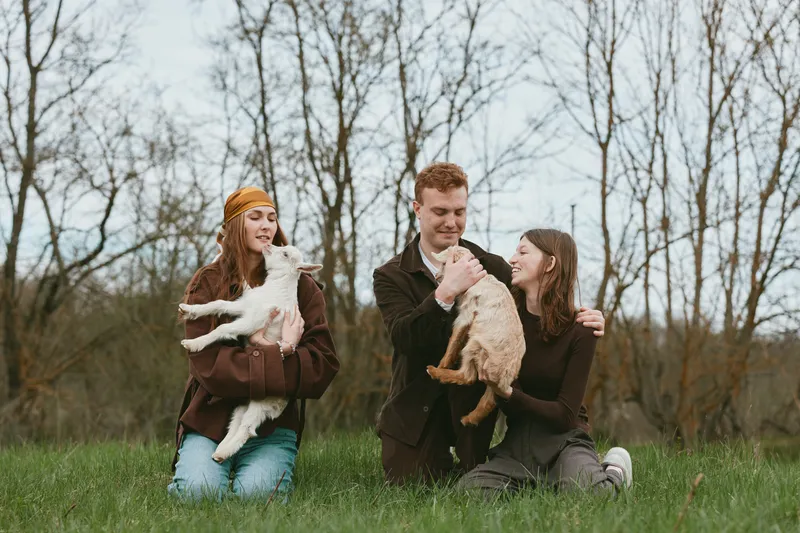 A joyful family sits on grass in a park, each parent holding a small dog, as a child smiles nearby. Candid lifestyle moment highlighting pets, bonding, and outdoor leisure.