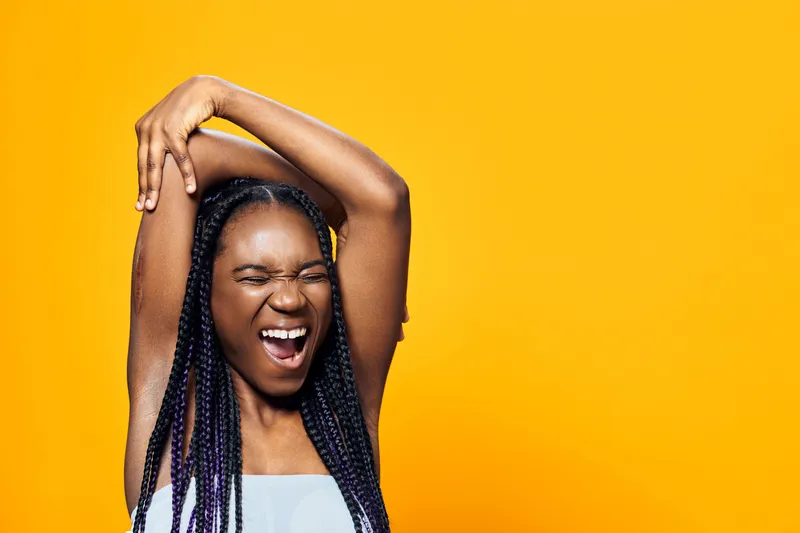 Joyful young Black woman stretching with enthusiasm against a vibrant yellow background, expressing happiness and vitality, ideal for wellness themes