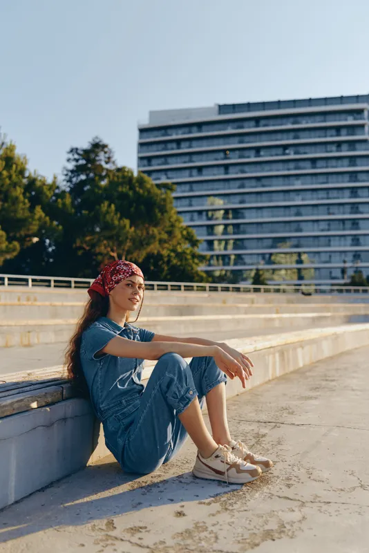 lifestyle woman in modern boho-western denim street style sitting outdoors with relaxed pose under bright natural light, film color aesthetic