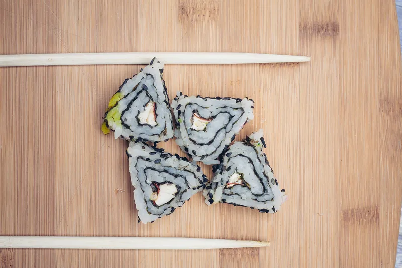 Треугольные роллы суши и палочки для еды на деревянном фоне, азиатская кухня