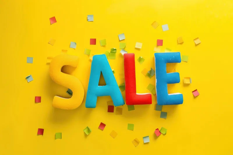 На желтом фоне разноцветные пластиковые буквы sale в окружении конфетти