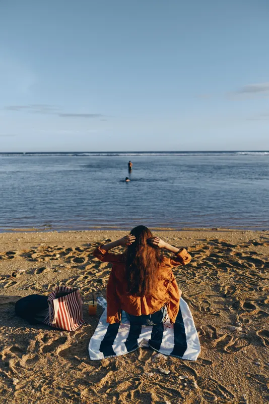 Dog on sandy beach sand relaxing on a blanket by the ocean, calm sea horizon with gentle waves, summer outdoors, soft sunrise sunlight, peaceful leisure