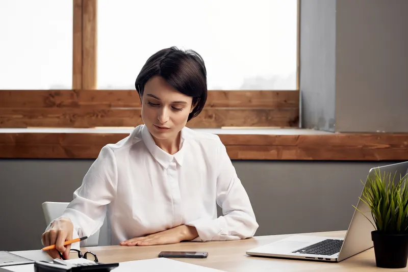 Женщина в костюме сидит перед ноутбуком с документами, профессиональная работа на изолированном фоне