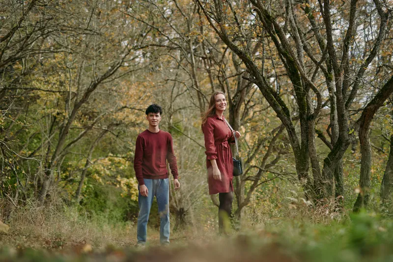 Two individuals stand in an autumn forest, facing forward with calm posture, conveying authenticity and credibility through natural pose and soft, earthy tones.