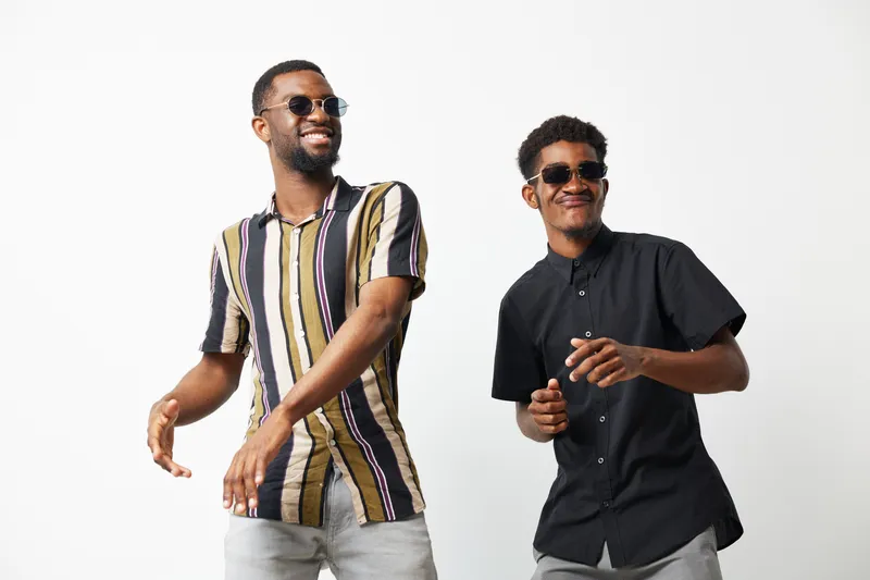 Two African American men enjoying a playful moment, wearing stylish sunglasses and trendy shirts. They exude joy and confidence with their smiles and energetic poses.