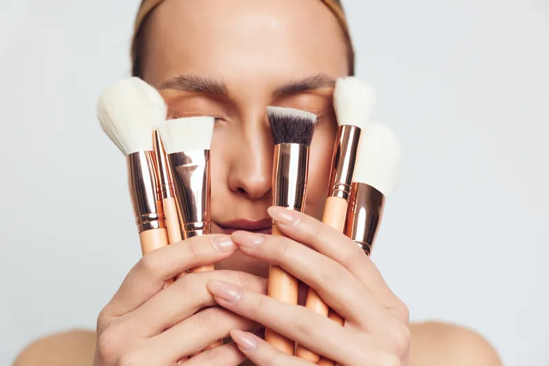 Close up portrait of woman applying makeup with professional brushes, covering cheeks and eyes, soft studio lighting, clean background, beauty routine, cosmetics application.