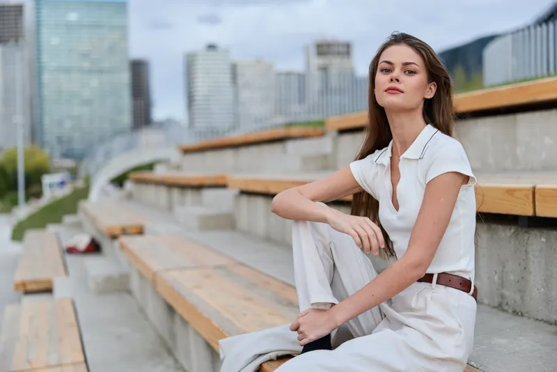 Confident woman in business attire sitting on outdoor bleachers, showcasing elegance and professionalism in an urban environment.