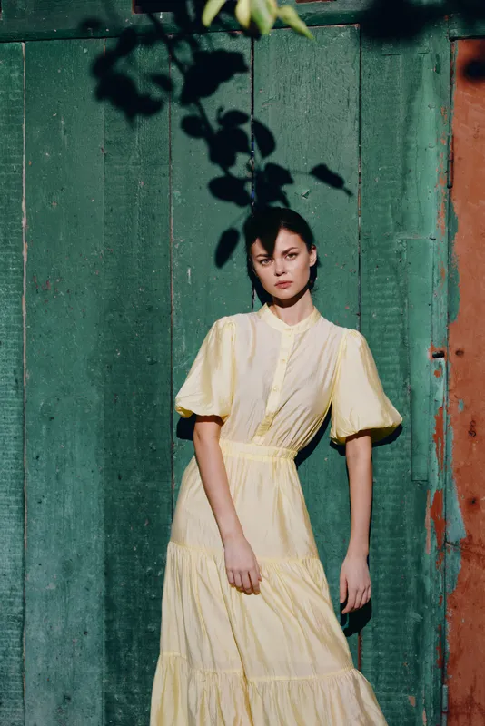 woman portrait in yellow vintage dress against green wooden wall sunlight and shadow, authenticity inclusivity mood
