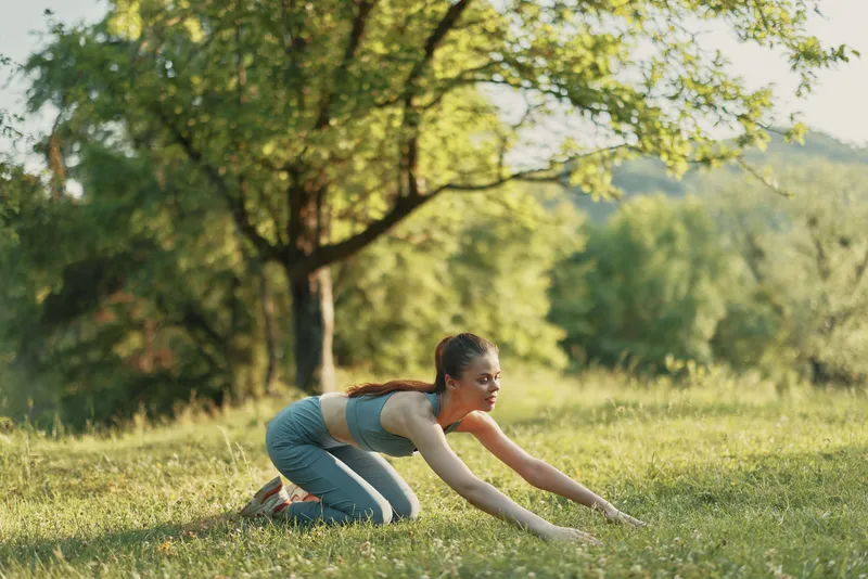 Young athletic woman practicing yoga in a serene green park, dressed in sportswear, expressing calmness and focus during a summer morning session