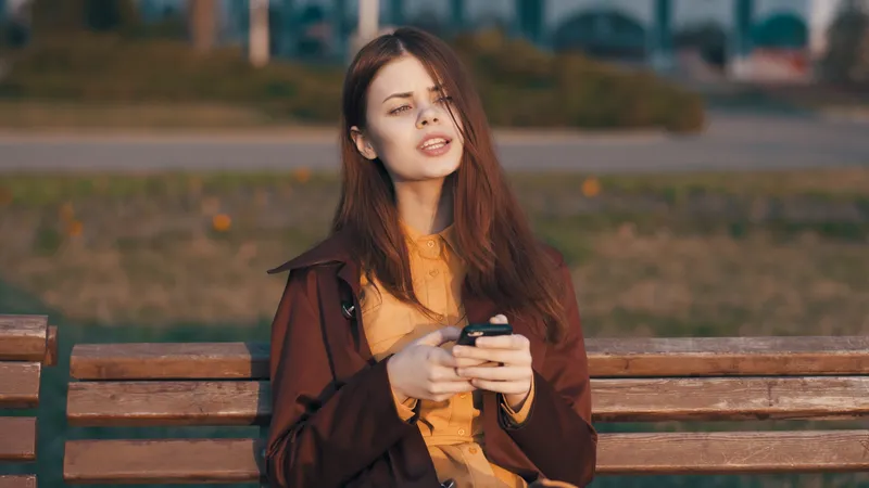 Женщина на улице на скамейке с телефоном в руке общается на свежем воздухе