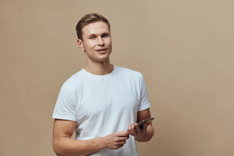 smiling young caucasian man hold smartphone use mobile phone casual white t-shirt beige background digital nomad concept