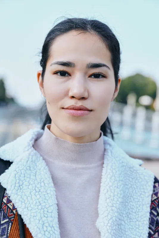 Female with calm expression outdoors in a textured coat, soft lighting, shallow depth of field, urban backdrop, natural style and candid mood