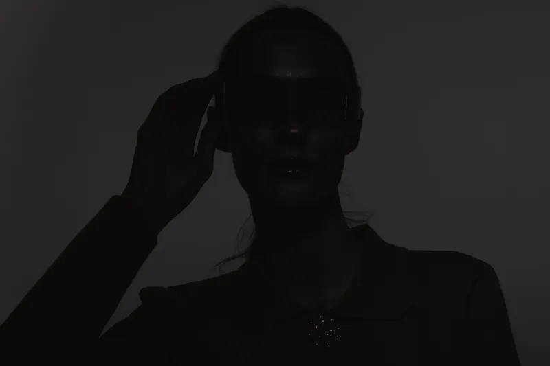 Portrait of a dark skin African woman wearing sunglasses and a dark outfit, posing confidently in studio lighting.