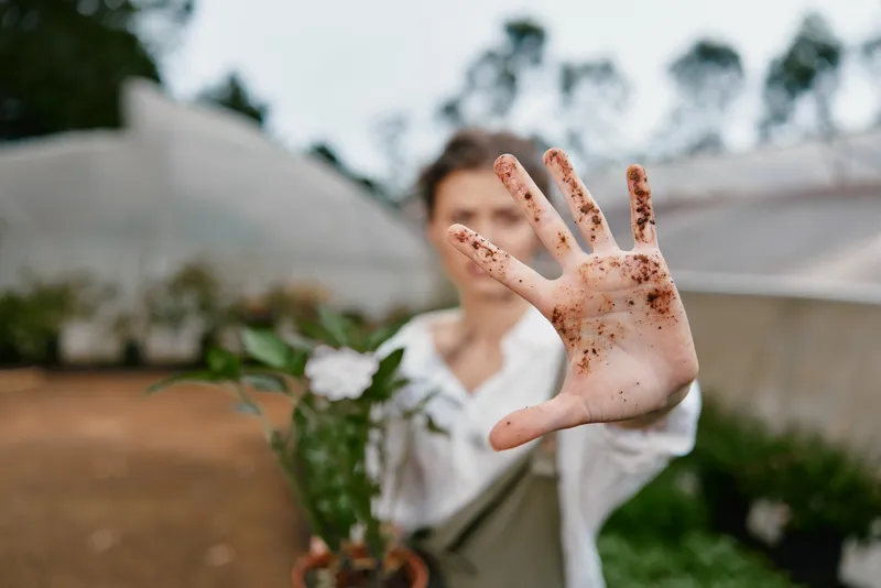 Young person in garden holding potted flower, showing dirty hands with soil green background evokes a connection to nature and gardening