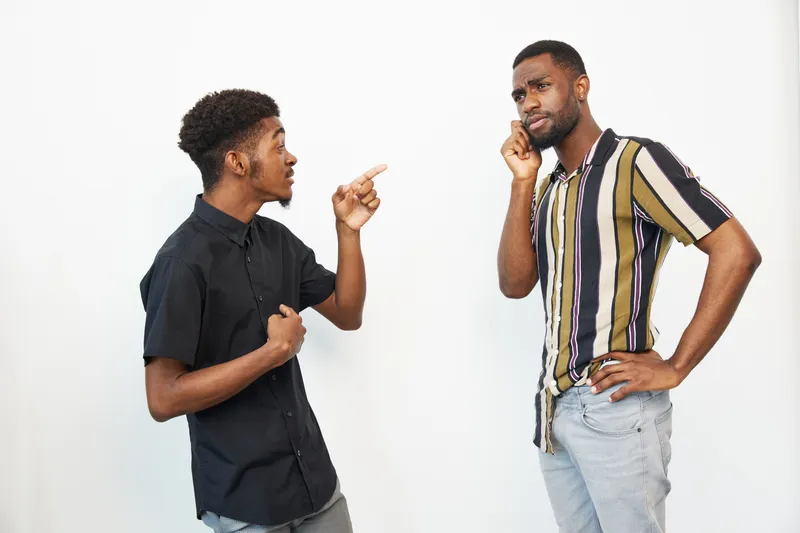 Two African American men engaged in a heated conversation, displaying strong emotions and contrasting facial expressions. The scene captures tension and dynamic energy.