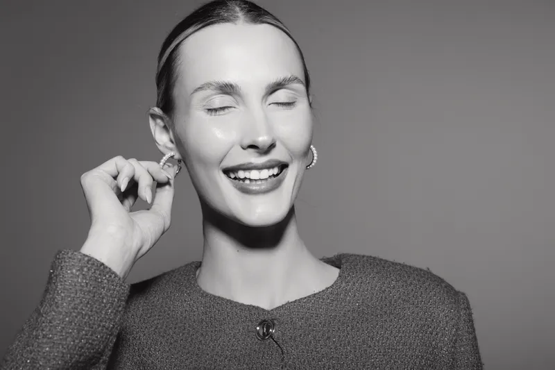 Smiling white woman with light skin and closed eyes touching earring. Black and white portrait. Concept of happiness, joy, and casual fashion style.