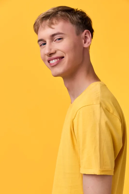 Smiling young man in a bright yellow t shirt against a solid yellow backdrop, showcasing casual fashion, studio lighting, and a cheerful vibe suitable for lifestyle branding and youth culture