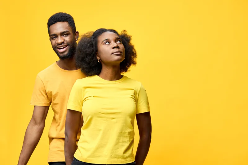 Cheerful young Black couple wearing matching yellow shirts, enjoying playful moments against a vibrant yellow background