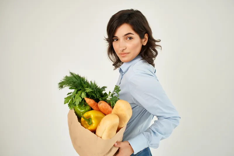 Милая брюнетка с пакетом продуктов на светлом фоне
