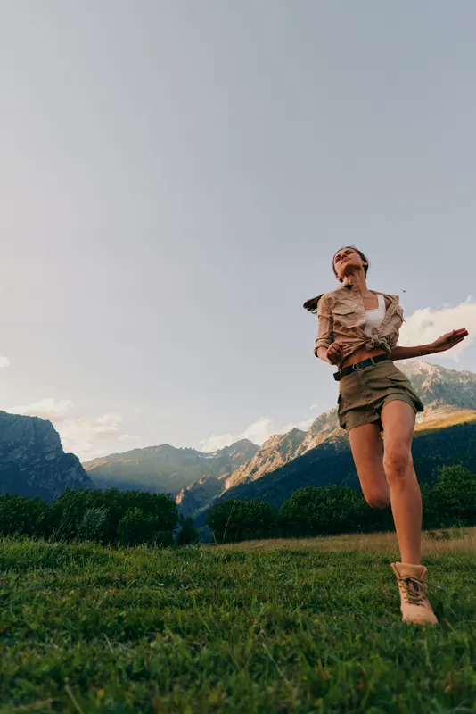 A carefree woman explores a sunny field with distant mountains, capturing a moment of outdoor living and joy. Concept includes freedom, nature, and healthy lifestyle.