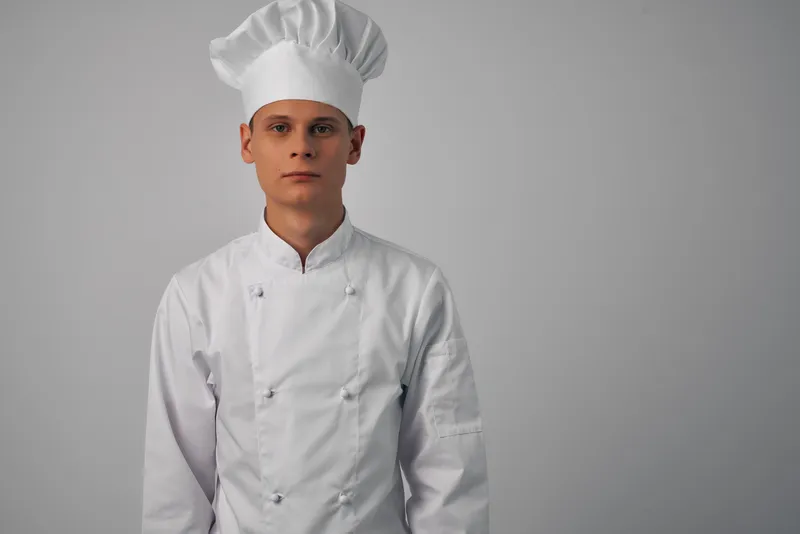 Весёлый шеф-повар мужского пола работает на кухне ресторана, занимаясь приготовлением блюд
