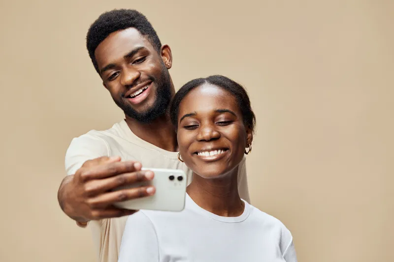 Happy African couple taking selfie together, showcasing joy and connection with warm background tones for lifestyle and relationship concepts