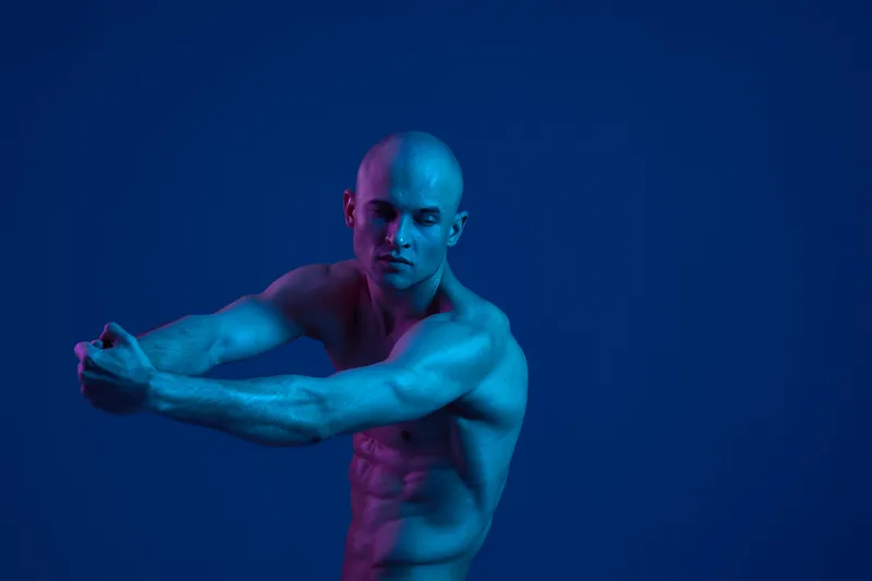 Fit man stretching against a vibrant blue background, showcasing strength and focus. The image radiates energy and determination, perfect for fitness-related content.