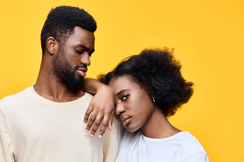 Young African couple displaying affection against a vibrant yellow background, showcasing intimacy and love in their expressions and attire