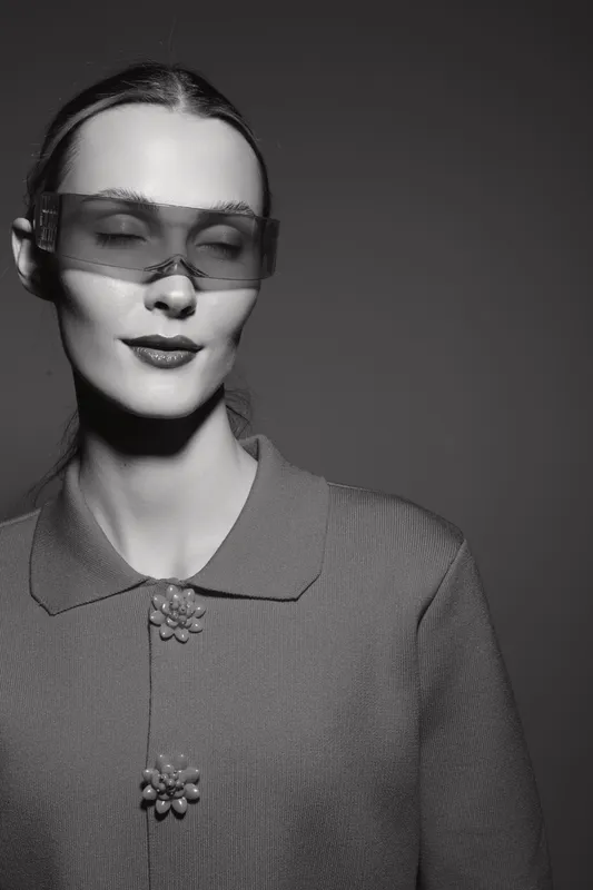 Portrait of a young caucasian woman with pale skin wearing transparent glasses and a textured shirt with decorative buttons. Studio lighting and minimalistic style.