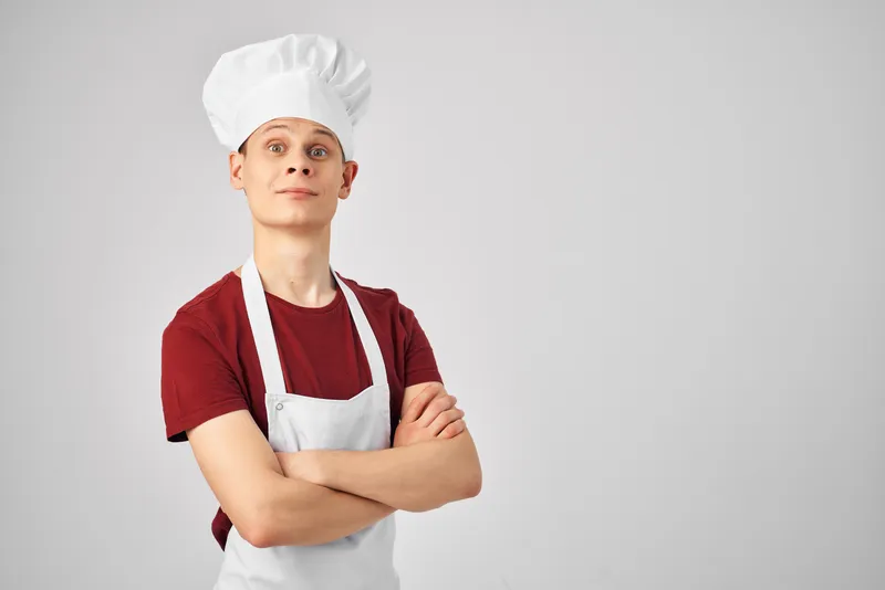 Повар-мужчина в белом фартуке и колпаке работает на светлом фоне