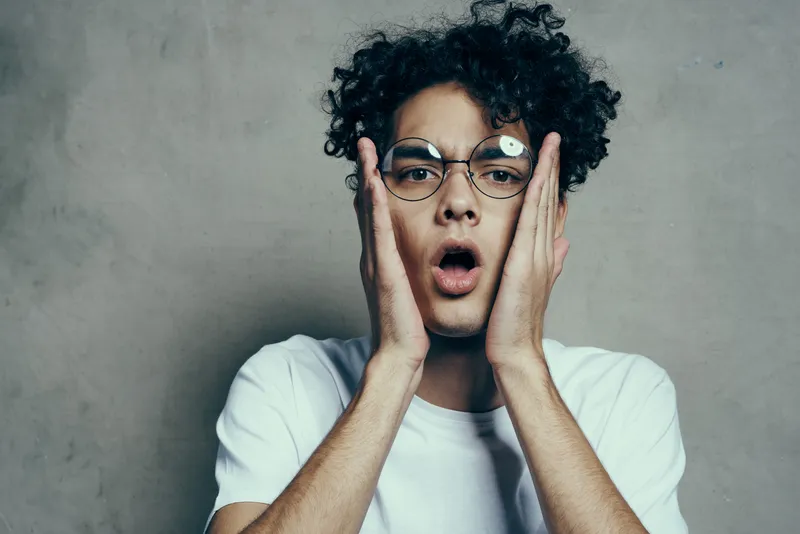 Крупный план мужчины с кудрявыми волосами в очках, демонстрирующего эмоции в студии