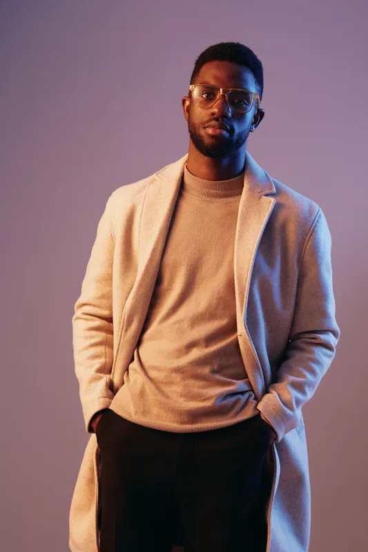 Stylish Black man in modern attire showcasing confidence in a soft, colorful background, perfect for fashion and lifestyle themes