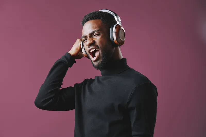 Young Black man singing passionately while wearing headphones against a purple background, showcasing emotions of joy and music appreciation
