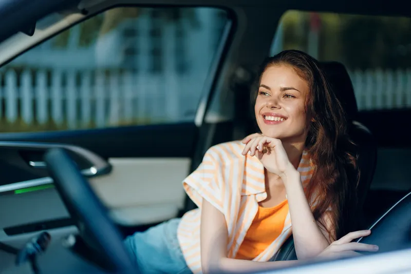 Счастливая женщина отдыхает в салоне автомобиля, улыбаясь и наслаждаясь моментом в солнечный день