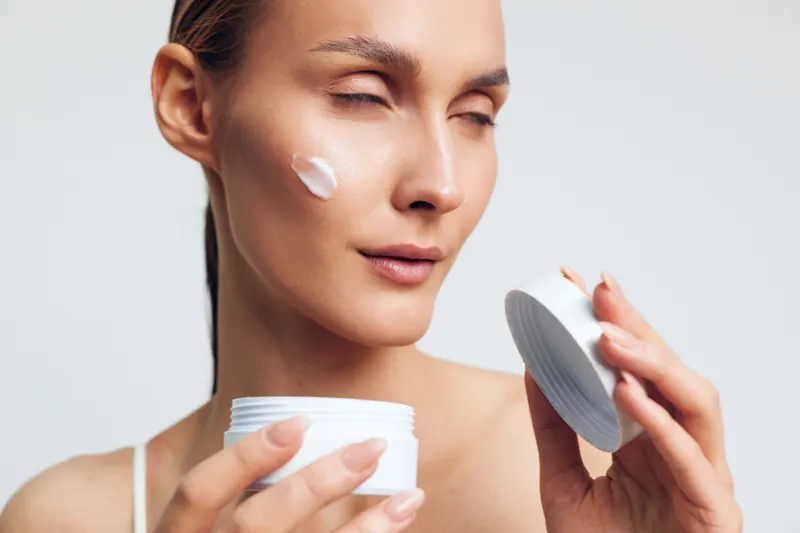 Calm skincare moment, woman applying moisturizer to her face, close up shot, creamy texture, soft glow, natural tones, minimal makeup, routine focus