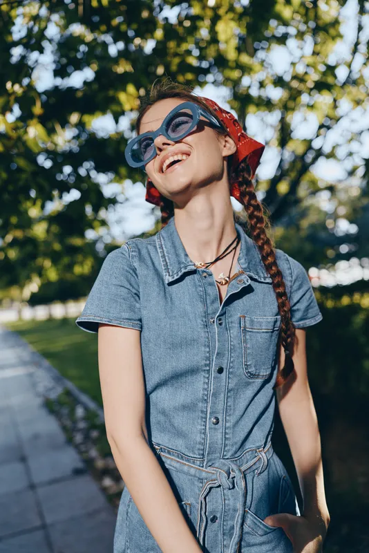 lifestyle woman wearing modern boho-western denim street style outfit with braided hair and sunglasses, enjoying sunny outdoor urban setting in film color tone